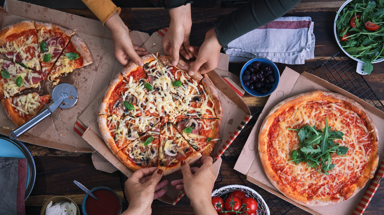 Hands reaching for pizza