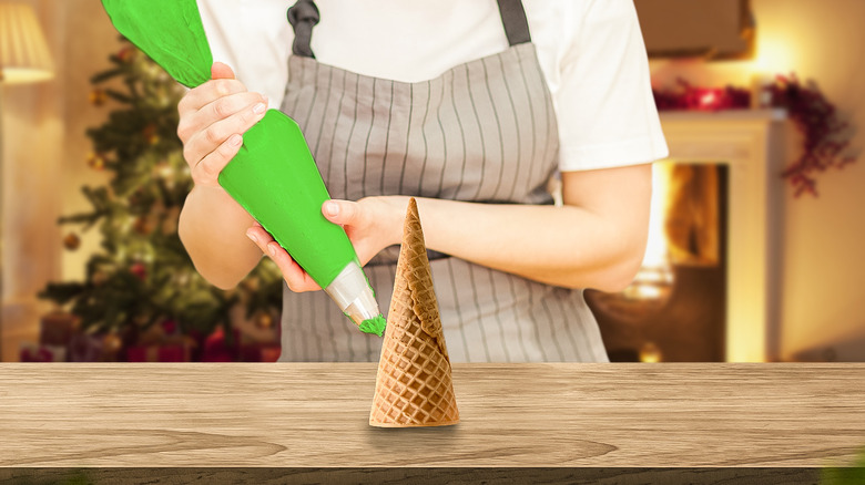 Hands putting green frosting on an upside down sugar cone