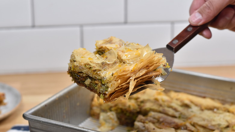 hand serving slice of baklava out of tray