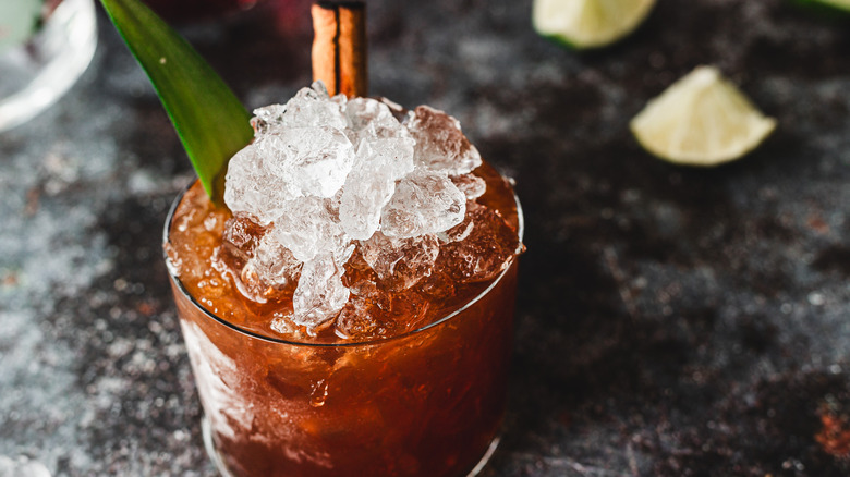 Red cocktail with ice and pineapple leaf, limes in back