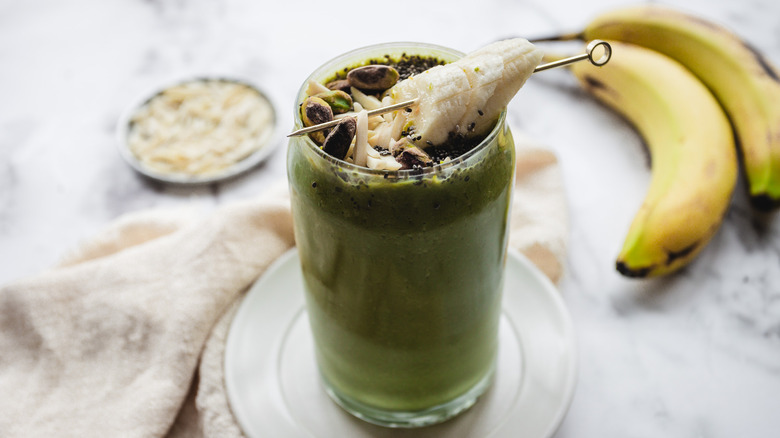 Green smoothie on white plate with bananas and almonds in background