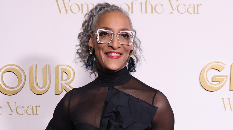 Carla Hall smiling in black dress and square glasses