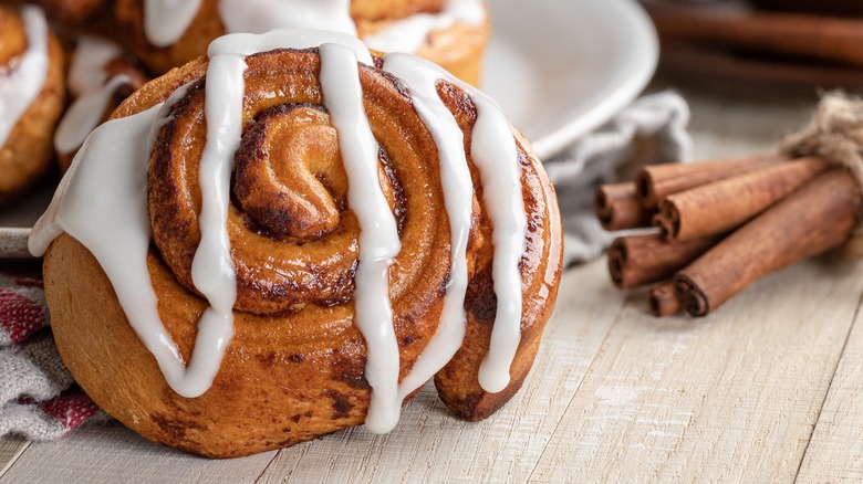 Closeup of a morning bun with icing next to cinnamon sticks