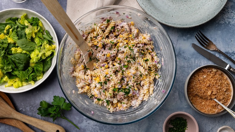 Top-down view of tuna pasta salad next to dishes of greens and toppings