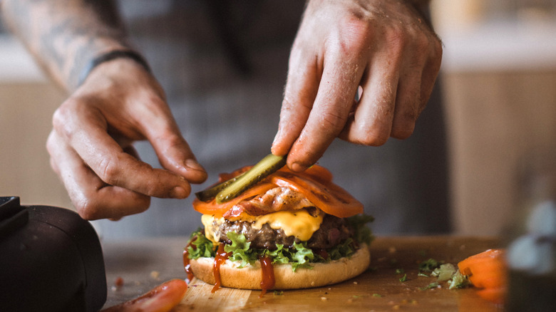 person adding pickles to burger