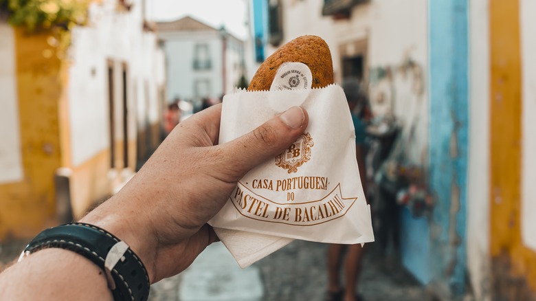 Outstretched hand holding cod fritter in paper sleeve