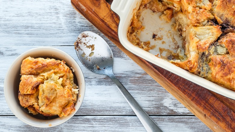 Top-down view of a dish of bread pudding next to a spoon and a piece in a bowl